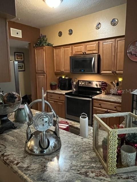 kitchen with electric range, light stone counters, and a textured ceiling