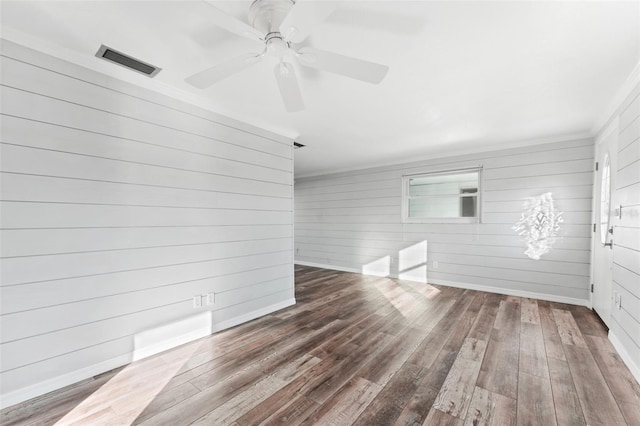 spare room with wooden walls, dark hardwood / wood-style flooring, ceiling fan, and ornamental molding