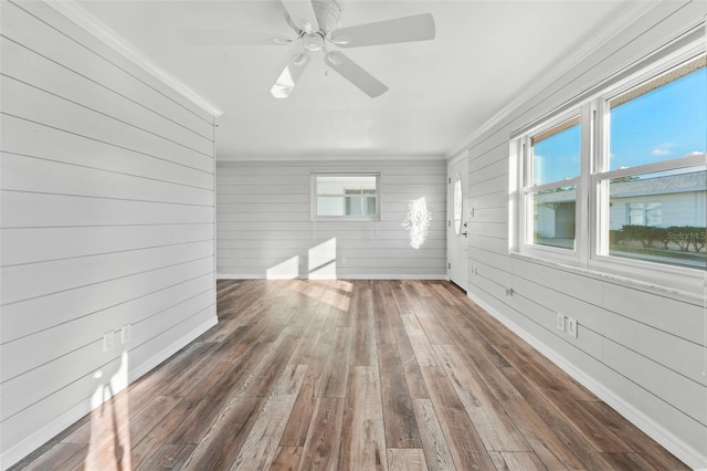 unfurnished room featuring wood walls, ceiling fan, dark wood-type flooring, and ornamental molding