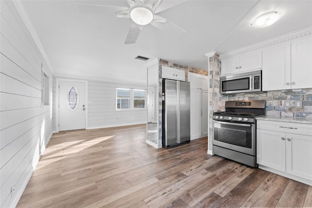 kitchen featuring hardwood / wood-style floors, wooden walls, decorative backsplash, white cabinetry, and stainless steel appliances