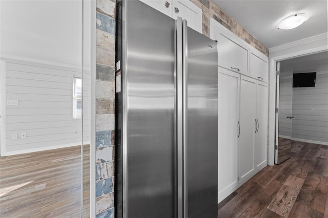 kitchen featuring white cabinets, wood walls, dark hardwood / wood-style flooring, and stainless steel refrigerator