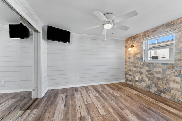 unfurnished room featuring wood walls, hardwood / wood-style floors, ceiling fan, and brick wall