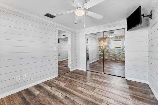 unfurnished bedroom with hardwood / wood-style floors, wooden walls, ceiling fan, and ornamental molding