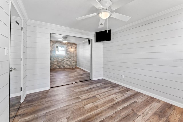 empty room with wood walls, wood-type flooring, and crown molding