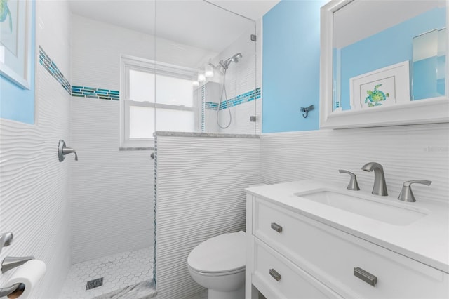 bathroom featuring a tile shower, vanity, toilet, and tile walls