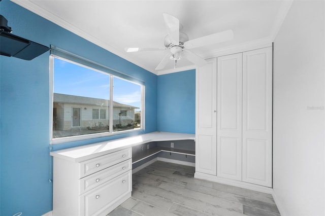 unfurnished office featuring ceiling fan, light hardwood / wood-style floors, built in desk, and ornamental molding