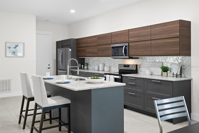 kitchen featuring appliances with stainless steel finishes, a kitchen breakfast bar, tasteful backsplash, a kitchen island with sink, and sink