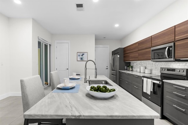 kitchen with appliances with stainless steel finishes, backsplash, a kitchen island with sink, and sink