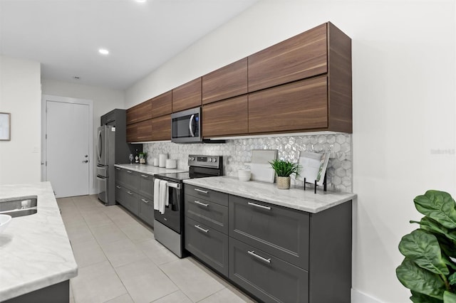 kitchen with backsplash, light stone countertops, light tile patterned floors, and appliances with stainless steel finishes