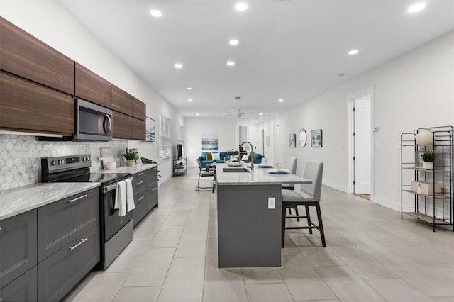 kitchen with ceiling fan, tasteful backsplash, a kitchen island with sink, a breakfast bar, and appliances with stainless steel finishes