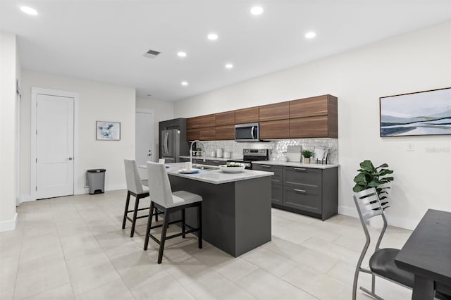 kitchen featuring appliances with stainless steel finishes, backsplash, a breakfast bar, a kitchen island with sink, and light tile patterned floors