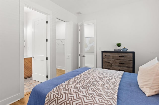 bedroom with a walk in closet, light hardwood / wood-style flooring, connected bathroom, and a closet