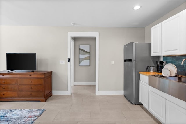 kitchen featuring decorative backsplash, white cabinetry, stainless steel refrigerator, and light tile patterned flooring