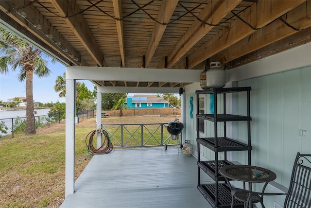 wooden deck featuring grilling area, fence, a water view, and a lawn