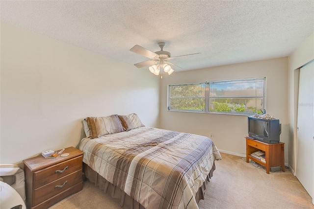 bedroom featuring ceiling fan, light colored carpet, and a textured ceiling