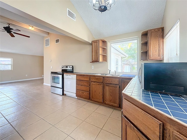 kitchen featuring a wealth of natural light, vaulted ceiling, stainless steel electric stove, tile countertops, and dishwasher