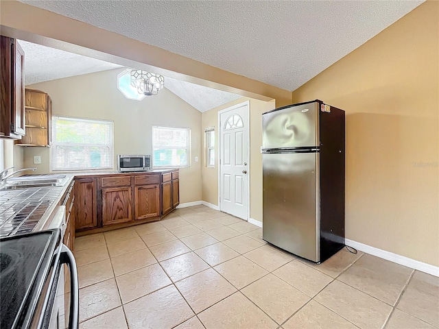 kitchen featuring appliances with stainless steel finishes, a textured ceiling, vaulted ceiling, and sink