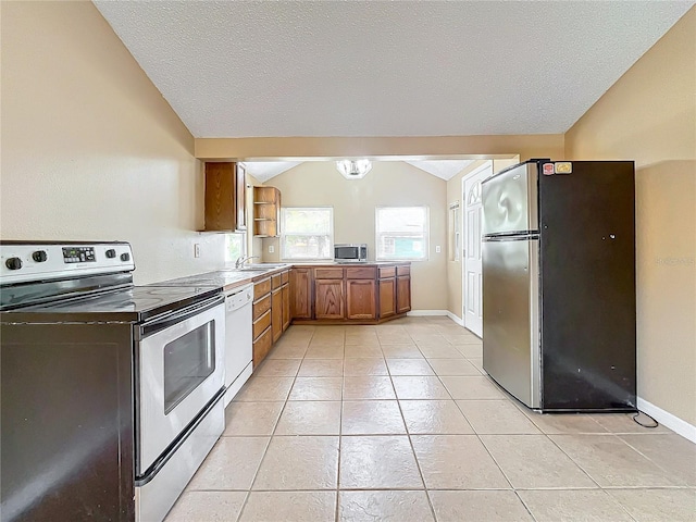 kitchen with a textured ceiling, stainless steel appliances, lofted ceiling, and light tile patterned flooring