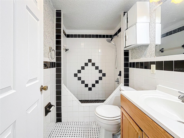 bathroom with vanity, toilet, a textured ceiling, tile walls, and a tile shower