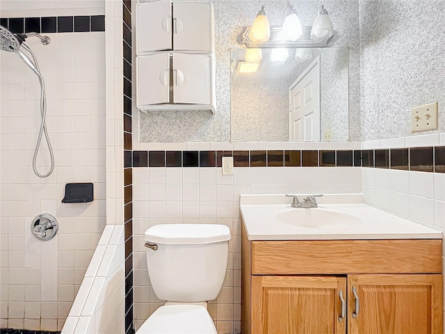 bathroom with tiled shower, vanity, toilet, and tile walls