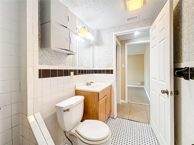 bathroom with a textured ceiling, vanity, toilet, and tile walls