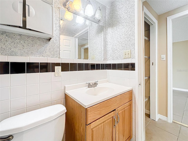 bathroom featuring vanity, a textured ceiling, tile walls, tile patterned flooring, and toilet