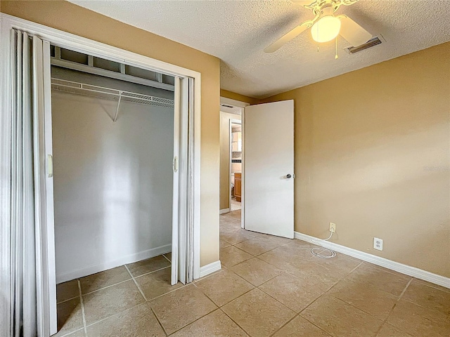 unfurnished bedroom featuring tile patterned flooring, a textured ceiling, a closet, and ceiling fan