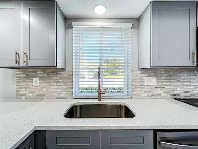 kitchen with gray cabinets, light stone counters, and sink