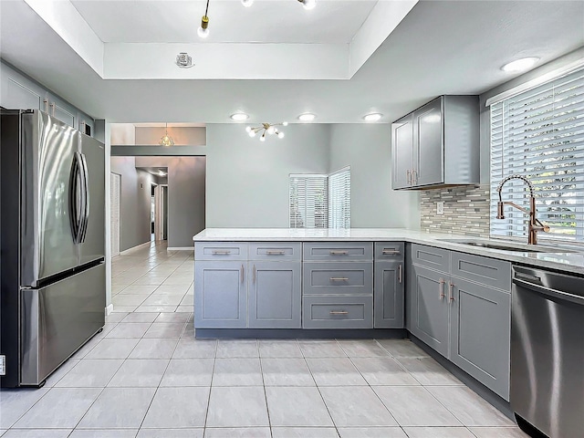 kitchen featuring kitchen peninsula, stainless steel appliances, gray cabinetry, and sink