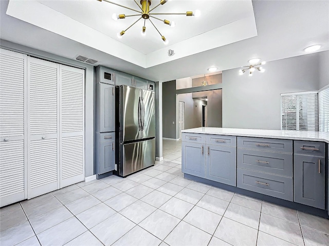 kitchen with gray cabinetry, an inviting chandelier, a raised ceiling, stainless steel fridge, and light tile patterned flooring