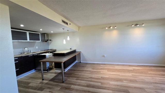 kitchen featuring pendant lighting, sink, wall chimney exhaust hood, a textured ceiling, and wood-type flooring