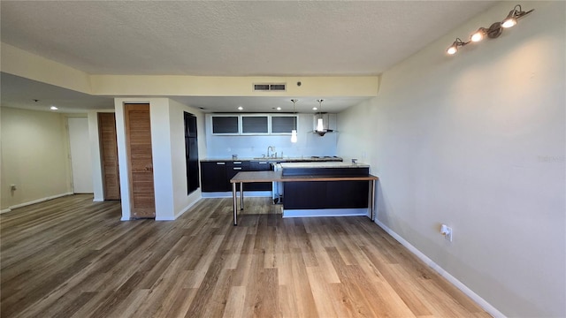 kitchen featuring sink, wall chimney exhaust hood, kitchen peninsula, a textured ceiling, and hardwood / wood-style flooring