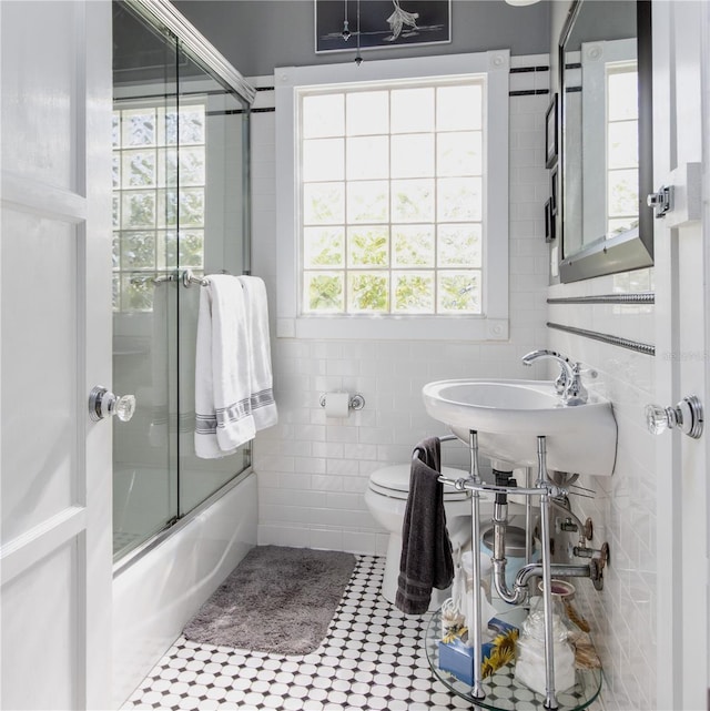 full bathroom featuring shower / bath combination with glass door, sink, tile walls, and toilet