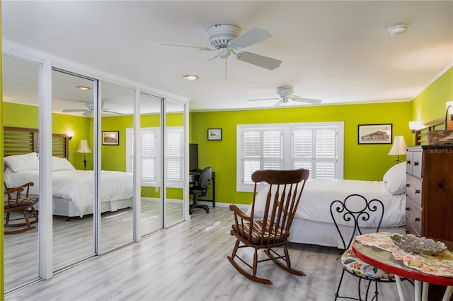 bedroom featuring ceiling fan, light hardwood / wood-style floors, ornamental molding, and multiple closets