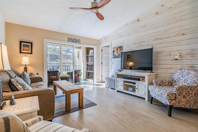 living room with ceiling fan, wooden walls, a textured ceiling, light hardwood / wood-style flooring, and lofted ceiling