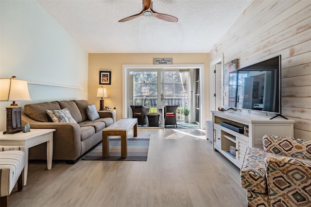 living room with a textured ceiling, ceiling fan, and light wood-type flooring