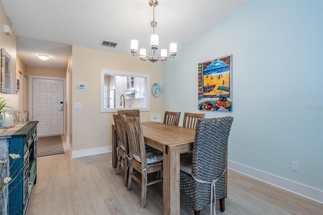 dining area featuring an inviting chandelier, a textured ceiling, and light hardwood / wood-style flooring