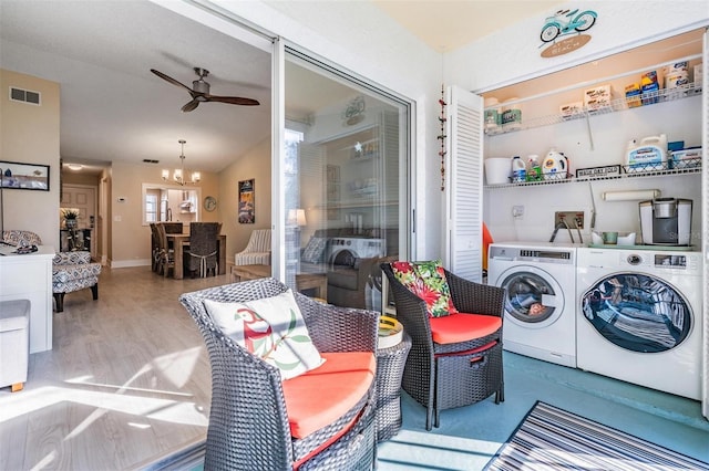 washroom featuring ceiling fan with notable chandelier, washing machine and clothes dryer, and light hardwood / wood-style flooring