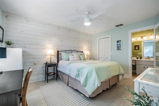 bedroom with ensuite bathroom, a textured ceiling, ceiling fan, light hardwood / wood-style floors, and a closet