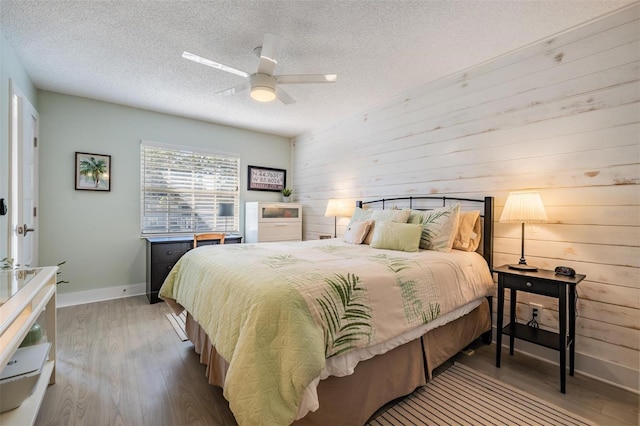 bedroom with wood-type flooring, wood walls, ceiling fan, and a textured ceiling