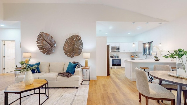 living room with vaulted ceiling, sink, and light hardwood / wood-style flooring