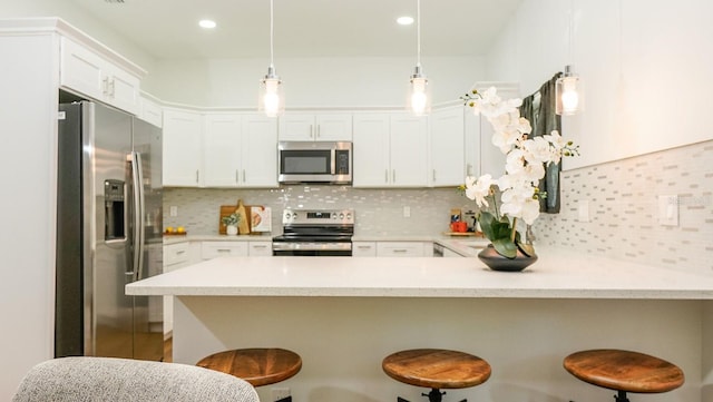 kitchen featuring hanging light fixtures, tasteful backsplash, a kitchen bar, kitchen peninsula, and stainless steel appliances