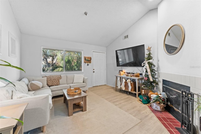 living room featuring hardwood / wood-style floors, lofted ceiling, and a tile fireplace