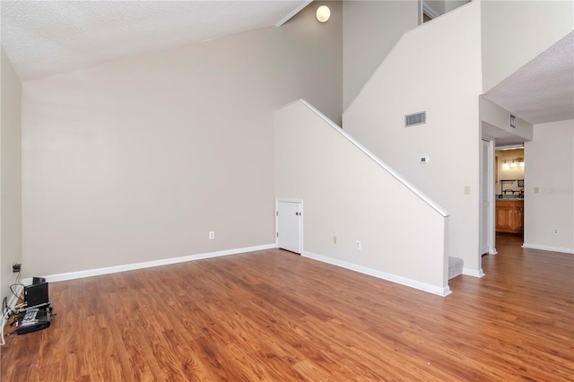 unfurnished living room with wood finished floors, visible vents, baseboards, and stairs