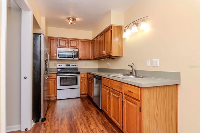 kitchen with dark wood finished floors, light countertops, appliances with stainless steel finishes, brown cabinetry, and a sink