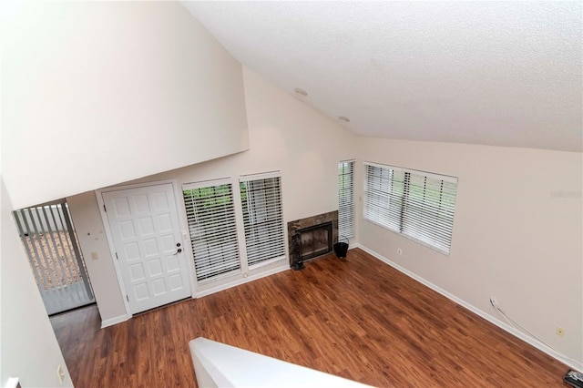 unfurnished living room with dark wood finished floors, lofted ceiling, a high end fireplace, a textured ceiling, and baseboards