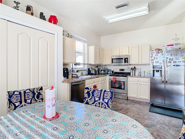 kitchen with cream cabinetry, appliances with stainless steel finishes, light stone counters, and sink