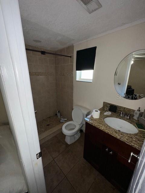 bathroom featuring toilet, a textured ceiling, a tile shower, tile patterned flooring, and vanity