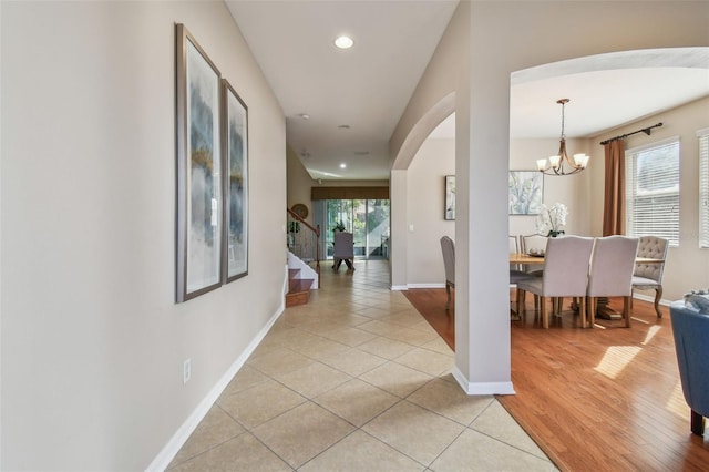 hallway with a wealth of natural light, light hardwood / wood-style flooring, and a notable chandelier