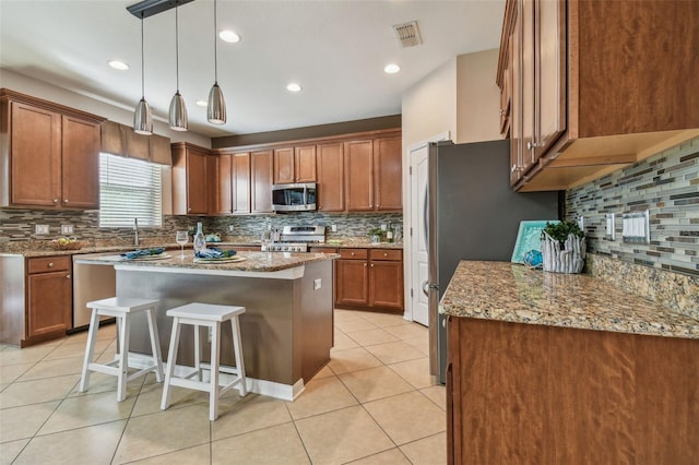 kitchen featuring a center island, backsplash, appliances with stainless steel finishes, light stone counters, and a breakfast bar area